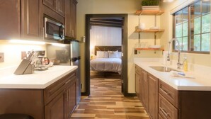 A kitchen with wooden cabinets, a microwave, and a coffee maker. There is a bed with white bedding in the background. - Unit 7 - Slide Rock Lodge (Sedona)