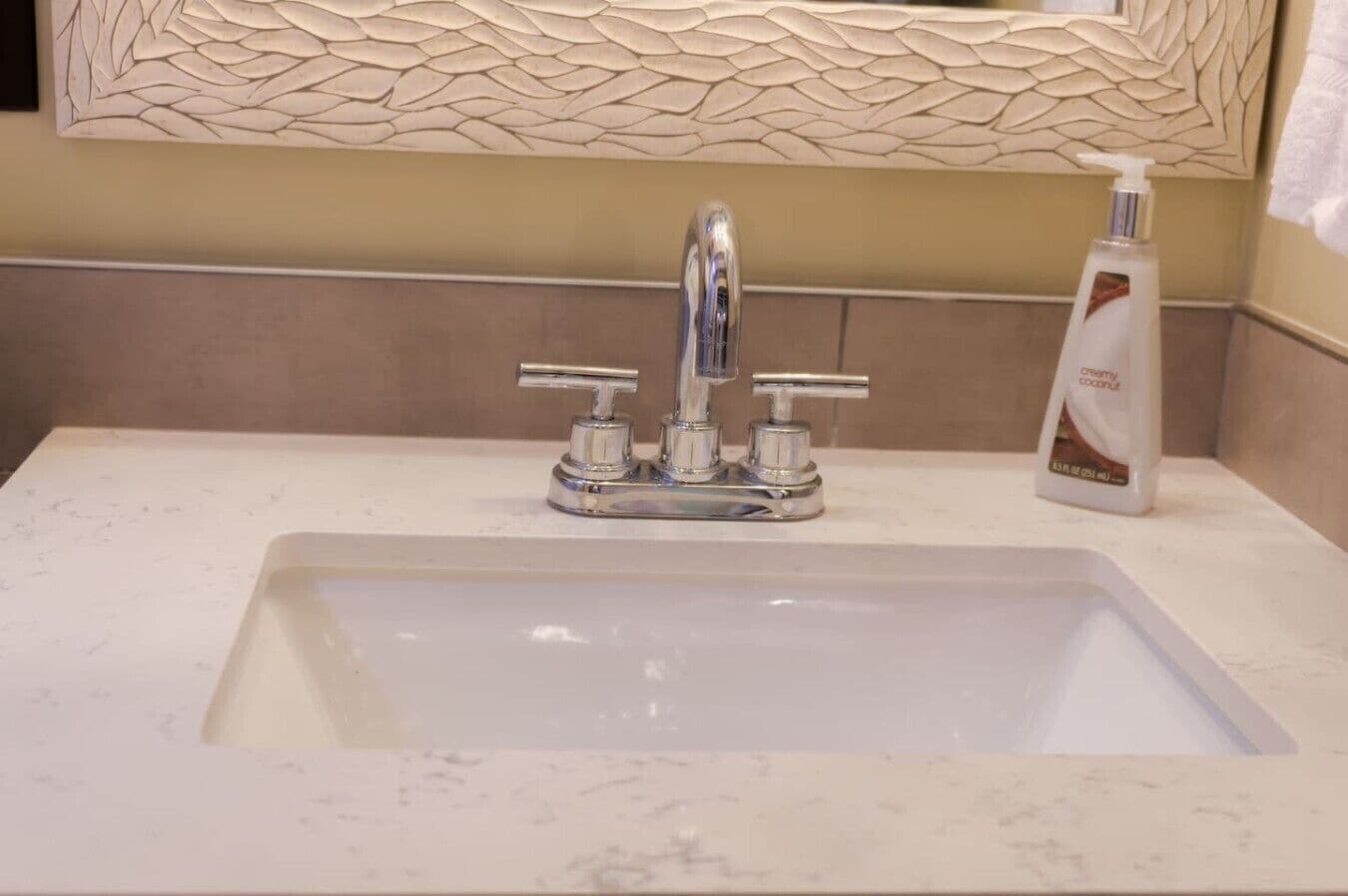 Un lavamanos de baño con un grifo moderno, una botella de loción y un panel decorativo en la pared.