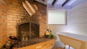 Ein Kamin aus Ziegelsteinen mit einer Holzherz-Dekoration, ein Fenster mit weißem Rollo und eine Badewanne.