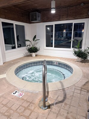 A hot tub with a 3 ft depth warning, surrounded by potted plants and large windows.