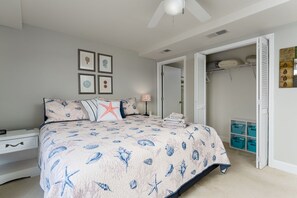 A bedroom with a bed, a nightstand, a bedside table, a lamp, a closet, and storage bins.