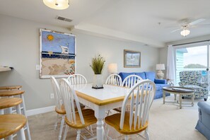 A dining area with a white table and chairs, a painting on the wall, and a view through the window.