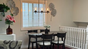 Un coin repas comprenant une table ronde, quatre chaises, un tapis rouge, un vase avec des fleurs et un élément décoratif mural.