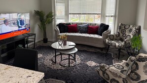 Un salon comprenant un téléviseur, un canapé, un fauteuil à motifs, une table basse et une plante en pot.