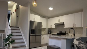 Une cuisine moderne dotée d’appareils électroménagers en acier inoxydable, d’un plan de travail en marbre et d’un escalier menant à un autre niveau.