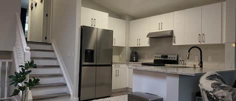 A modern kitchen with stainless steel appliances, a marble countertop, and a staircase leading to another level.