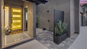 Una entrada de edificio moderna con una puerta amarilla, una maceta negra con plantas y un muro con diseño.