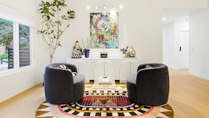Una sala de estar moderna con dos sillones grises, una mesita de centro, un cuadro abstracto colorido y una planta grande.