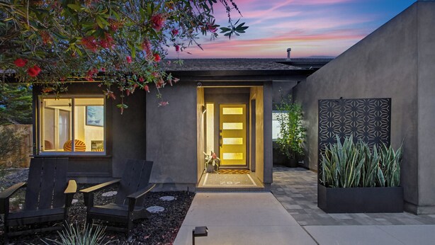 Una casa moderna con una entrada bien iluminada, mobiliario exterior y vistas al cielo.