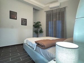 Ein Schlafzimmer mit Bett, Pflanze, Fenster mit Vorhängen und Klimaanlage.