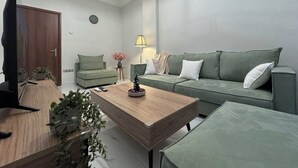 Una sala de estar moderna con una mesa de centro de madera, un sofá verde y un televisor sobre un mueble de madera.