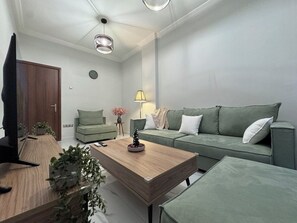 Ein modernes Wohnzimmer mit einem Holztisch, einem grünen Sofa und einem Fernseher auf einem Holzständer.