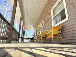 A covered porch with wooden railings, wicker chairs, and a view of the house.
