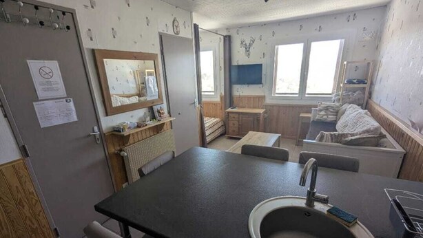 Ein kleines Zimmer mit Waschbecken, Spiegel, Tisch und Bett.