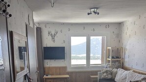 Ein kompakter Wohnbereich mit Küchenzeile, Essbereich, Sofa und einem großen Fenster mit Blick ins Freie.