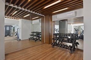 Ein Fitnessraum mit Holzböden, Spiegelwänden und unterschiedlicher Trainingsausstattung.
