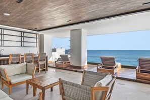 A spacious outdoor seating area with a view of the ocean, wooden furniture, and a modern kitchen in the background. - Malecón | Amplio | Torre de Lujo (Mazatlán)