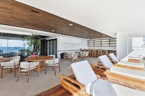 Een ruime binnenruimte met een houten plafond, een grote tafel met stoelen en verschillende comfortabele fauteuils.