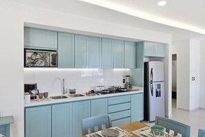 Une cuisine moderne avec des meubles de couleur bleu clair, un réfrigérateur en acier inoxydable et un coin repas comprenant une table et des chaises.
