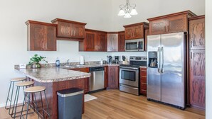 Eine Küche mit Holzausstattung, Edelstahlgeräten, einer Granit Arbeitsplatte und einer Bar.