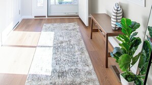Ein heller Korridor mit Holzboden, einem grauen Teppich, einer Bank und einer Topfpflanze.