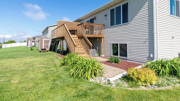 Ein zweigeschossiges Haus mit einer Holzterrasse, einer kleinen Außenküche und einem angelegten Garten.