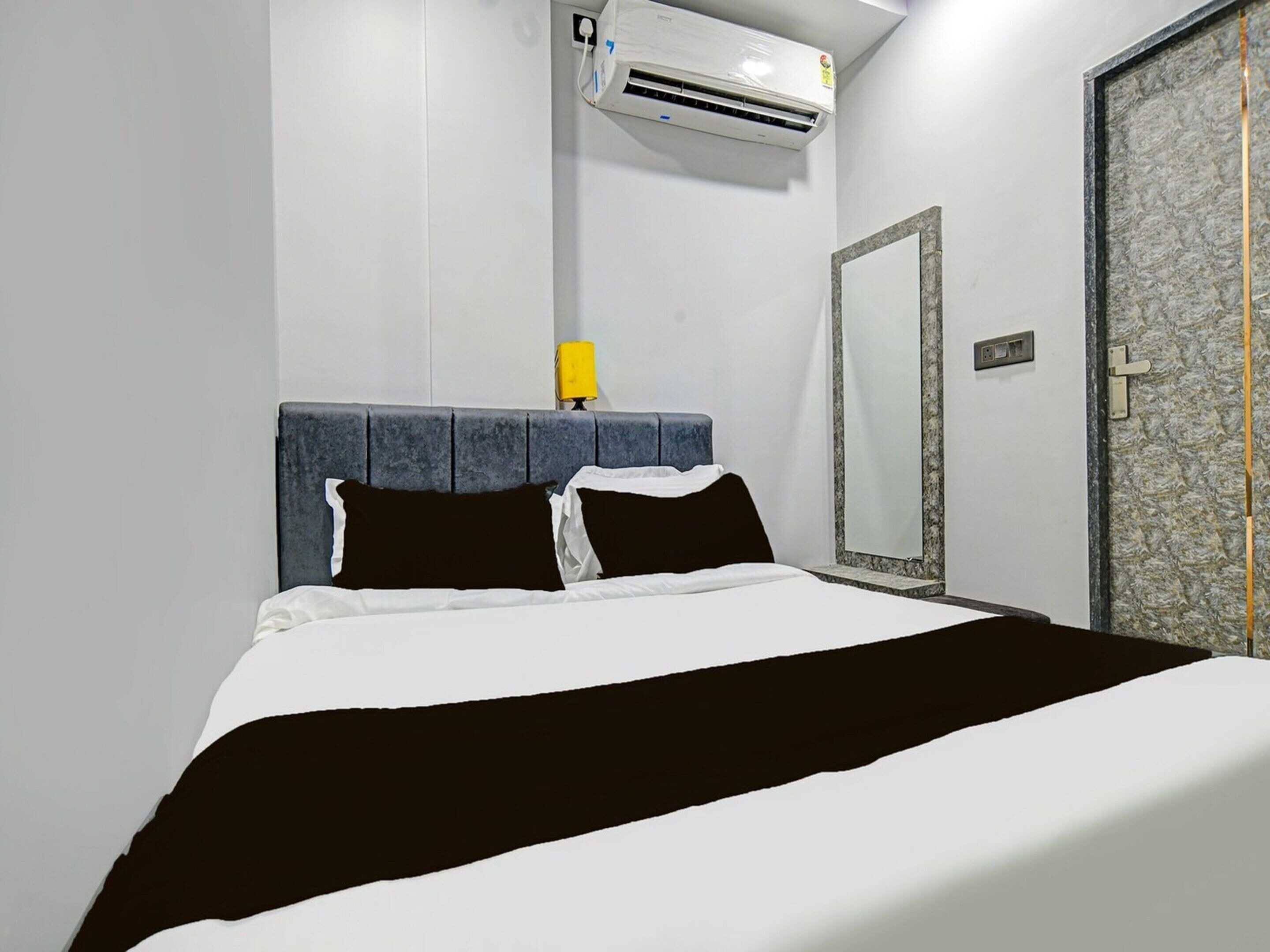 A hotel room with a bed, an air conditioning unit, a mirror, and a door.