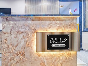 A reception desk with a marble-like design, a sign indicating 'Collection' and 'Company Serviced', and a vertical light fixture above. - Premium Hotel Maharana Pratap (Ujjain)
