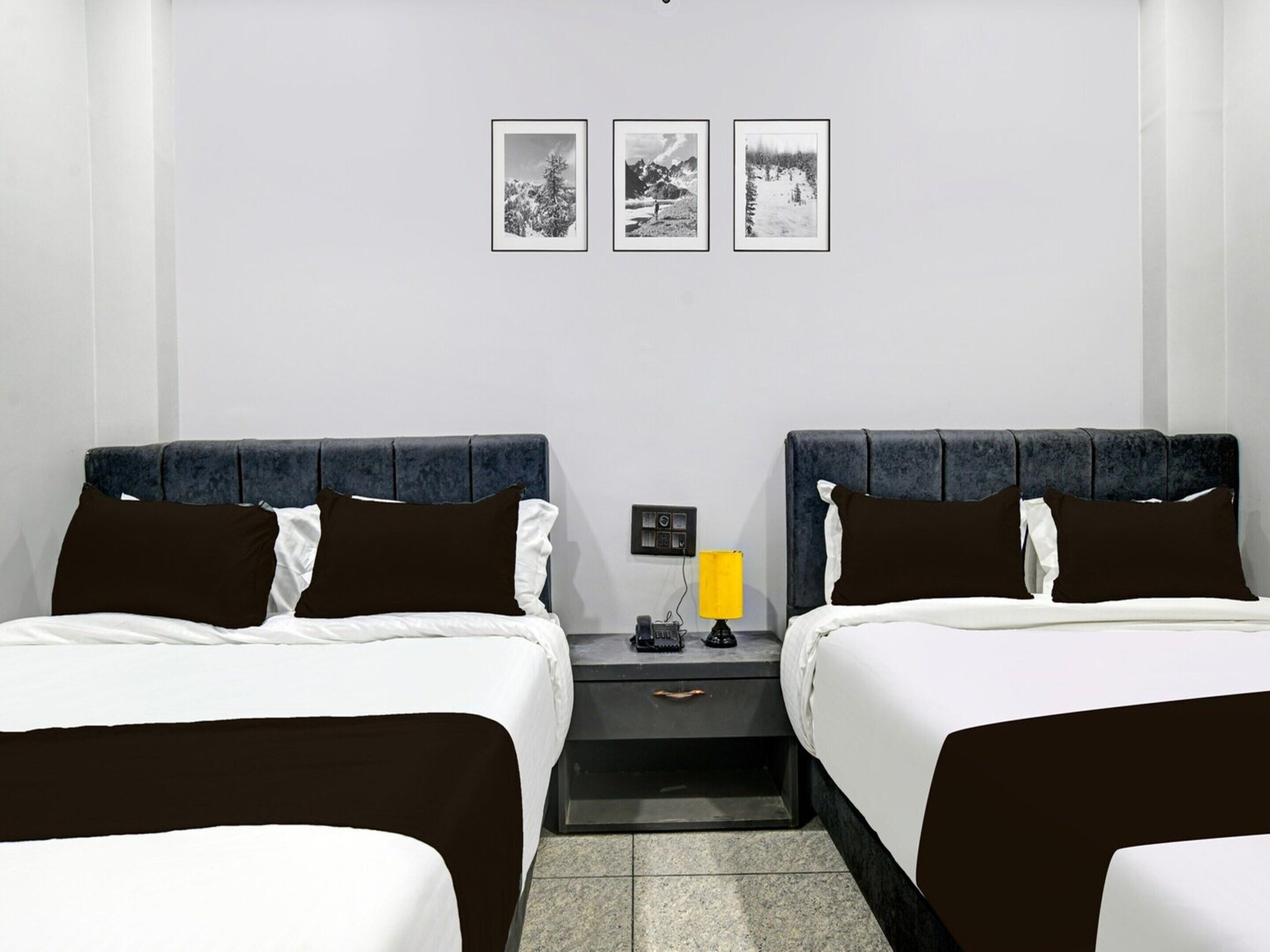 Habitación de hotel con dos camas, una mesita de noche con lámpara y tres cuadros enmarcados en la pared.