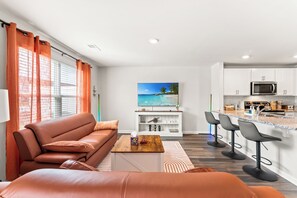 A modern living room with a sofa, a coffee table, and a TV. Adjacent is a kitchen with a microwave, cabinets, and bar stools. - Modern 3BR Townhouse w/ Porch Near Beach & Golf - Surfside Beach (Surfside Beach)