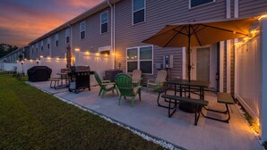 Un patio con mobiliario exterior, una parrilla y luces colgantes.