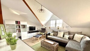 Ein modernes Loft-Apartment mit hohen Decken, einem Essbereich, einem Wohnzimmer mit Sofa und Fernseher sowie einer Küchenzeile.