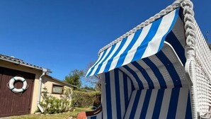 Ein Strandstuhl mit blau-weiß gestreiftem Muster, Holzrahmen und einer Metall-Armlehne.
