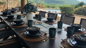 Un'area pranzo all'aperto con un tavolo lungo apparecchiato per un pasto, circondato da sedie, con vista su una montagna e una piscina sullo sfondo.