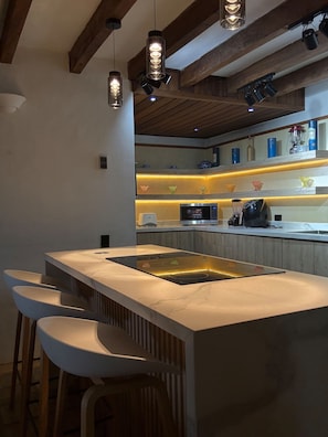 A modern kitchen with a central island, bar stools, pendant lighting, and wooden beams.