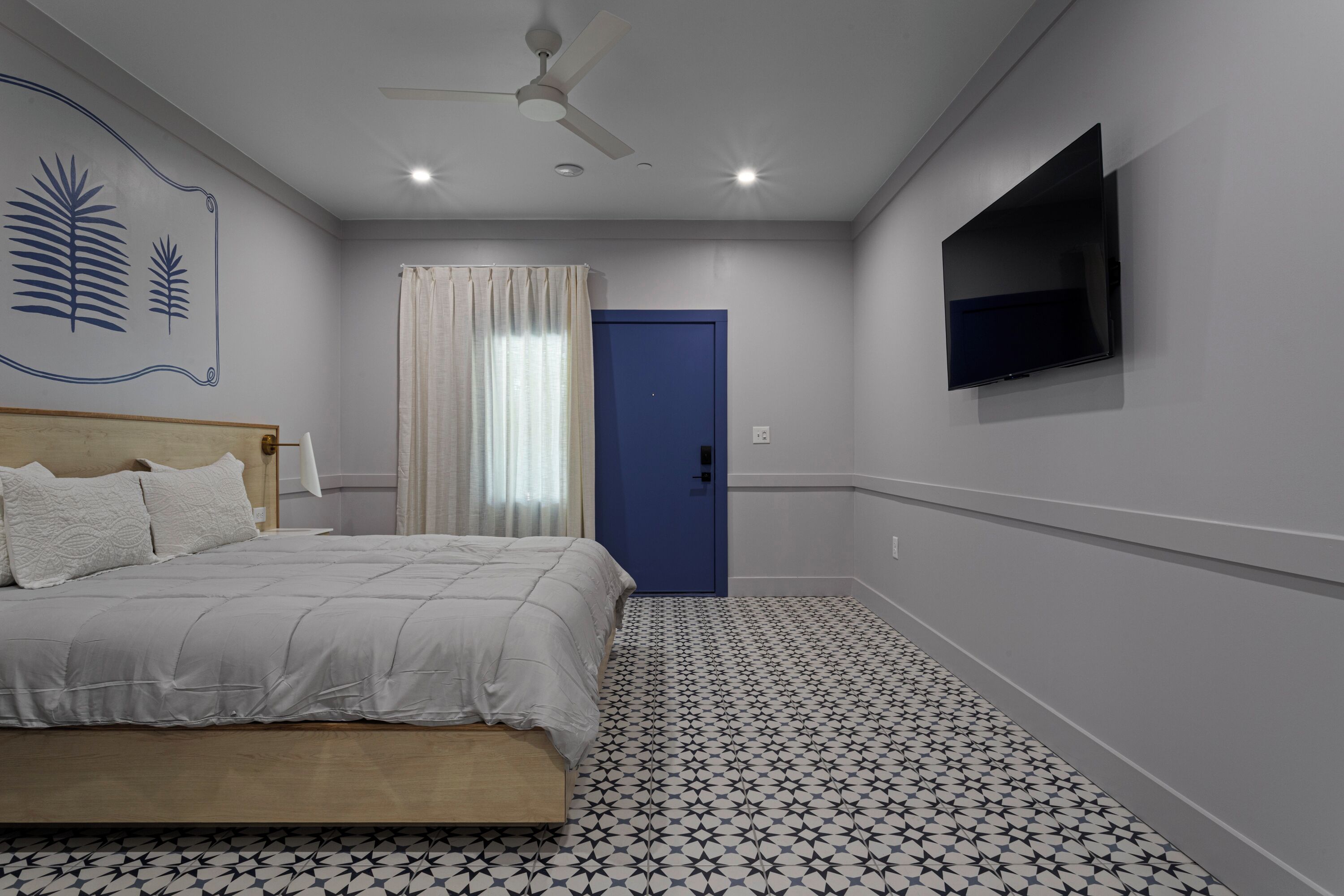 Ein Schlafzimmer mit einem Bett, einem Deckenventilator, einem an der Wand befestigten Fernseher und einem gestreiften Boden.