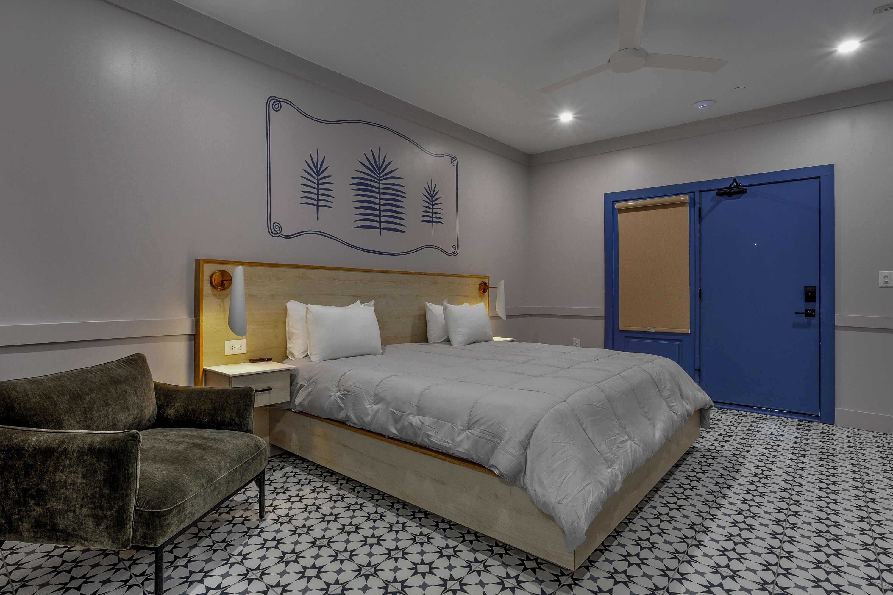 Un dormitorio con cama, mesita de noche, una silla, una puerta azul y un adorno en la pared.