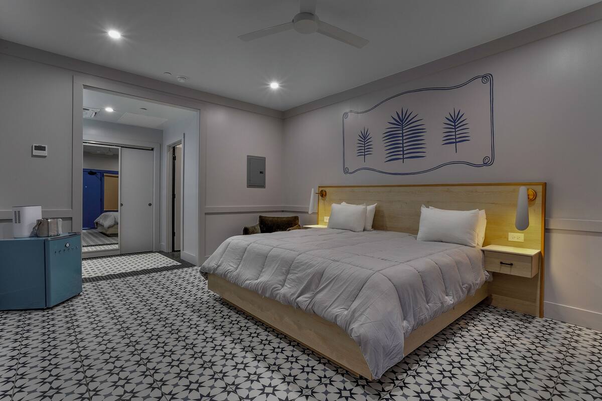 Un dormitorio con cama, mesitas de noche, ventilador de techo y piso estampado.