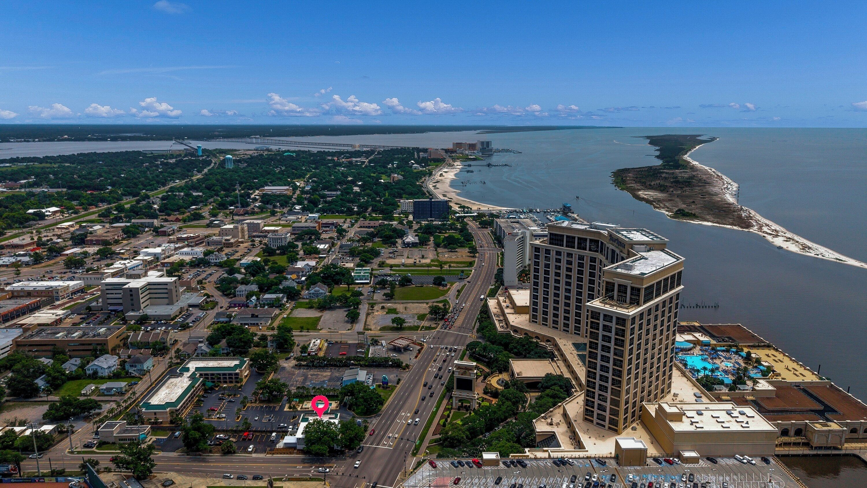 An aerial view of a coastal city with a prominent hotel featuring a rooftop pool and a view of the ocean.