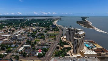An aerial view of a coastal city with a prominent hotel featuring a rooftop pool and a view of the ocean.