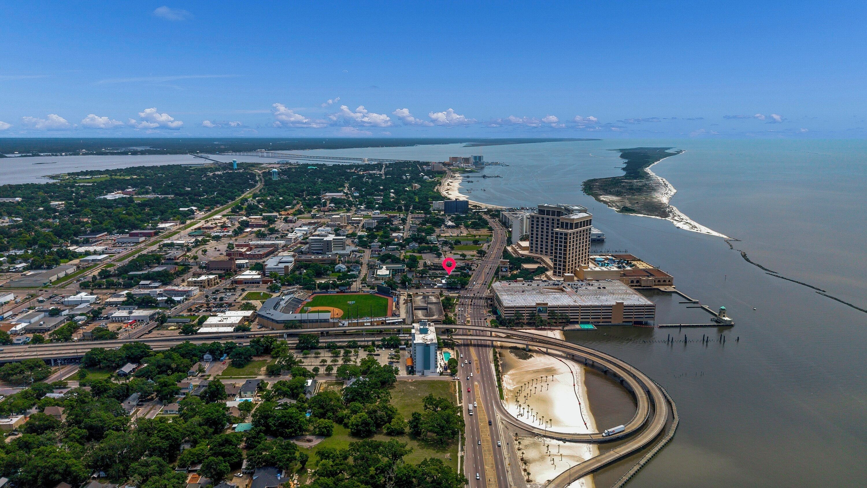 An aerial view of a coastal city with a prominent bridge, a marina, and a large hotel with a helipad.