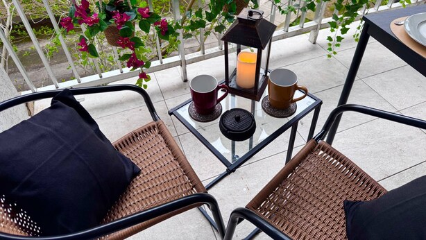 En balkon med fletstole, et bord med et lys og hængende planter.