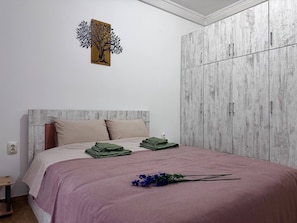Un dormitorio con cama, almohadas, cabecera de madera, armario y una obra de arte en la pared.