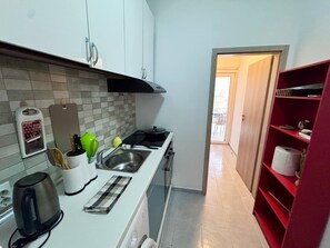 Una cocina compacta con un lavamanos, estufa y una unidad de almacenamiento roja.