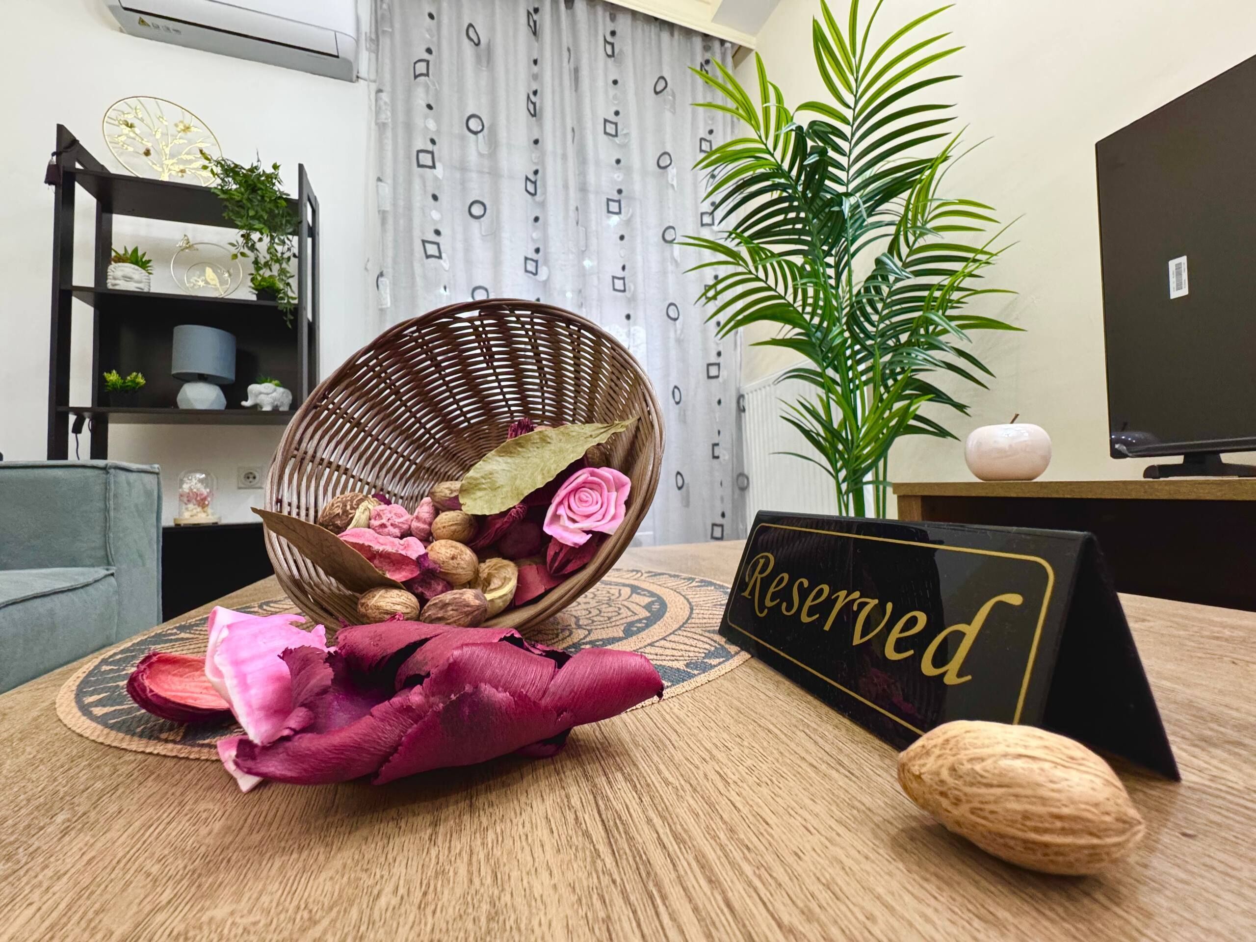 Un panier en osier contenant des fleurs séchées et des noix, placé sur une table, un panneau indiquant « Réservé », une plante en pot et un téléviseur posé sur un meuble.