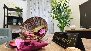 En fletkurv med tørrede blomster og nødder på et bord, et skilt med 'Reserved', en potteplante og et fjernsyn på et stativ.