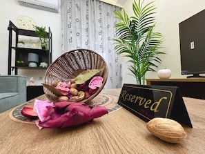 Una cesta de mimbre con flores secas y nueces sobre una mesa, un cartel que dice 'Reserved', una planta en maceta y un televisor sobre un pedestal.