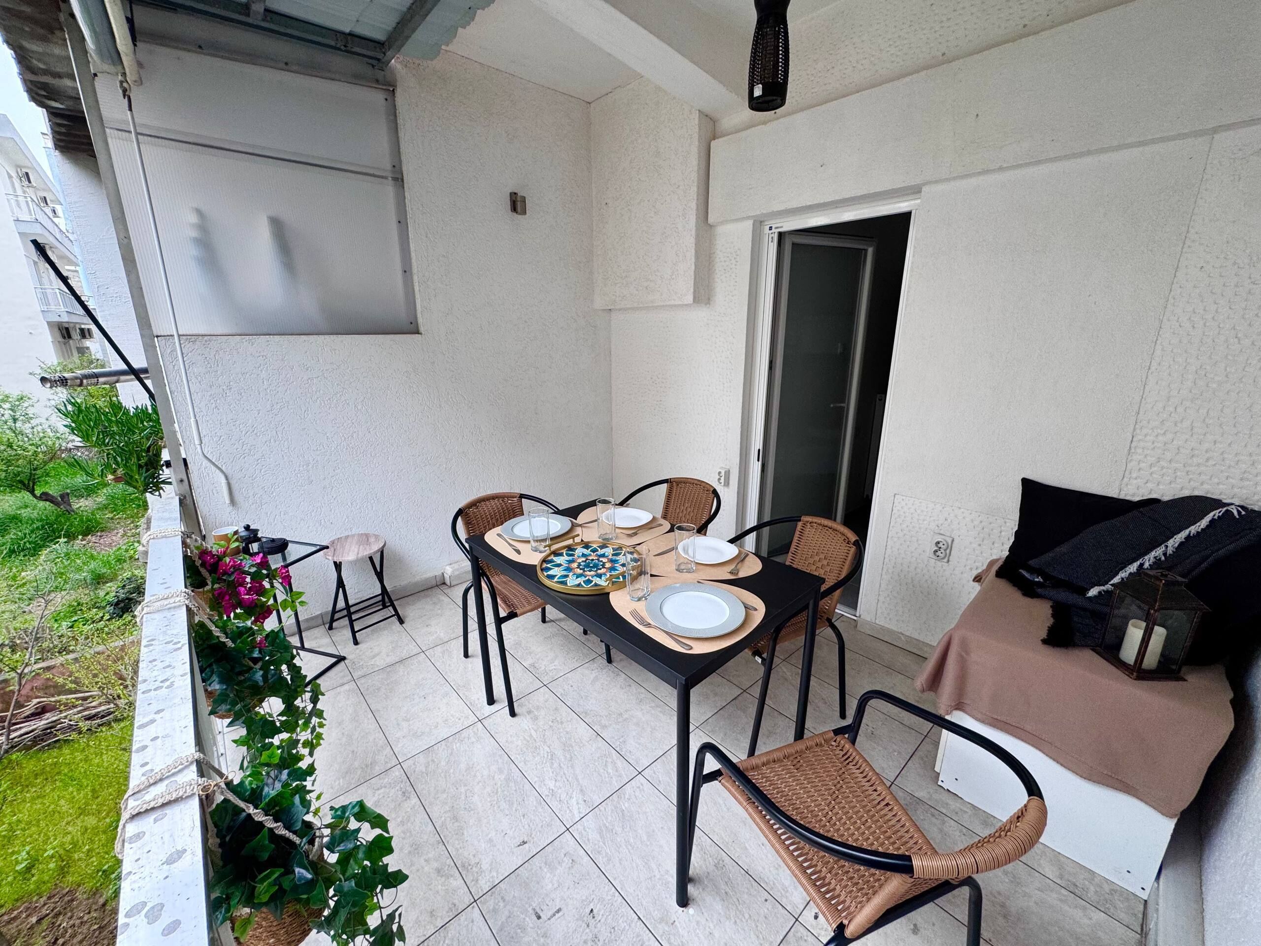 Een balkon met een tafel voor vier personen, omringd door rieten stoelen, een klein bijzettafeltje en een bank met kussens.