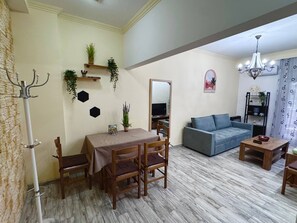 Una sala de estar con una mesa de comedor, sillas, un sofá, un televisor y una araña.