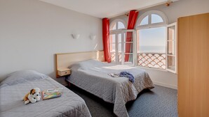 Quarto de hotel com duas camas, varanda com cortinas vermelhas e vista para o mar.